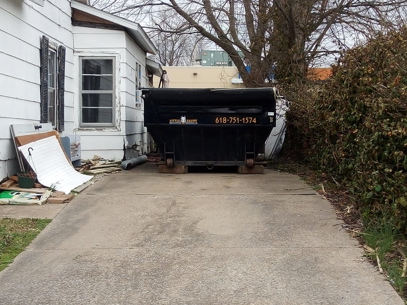 Little Egypt dumpster on a paved driveway beside a house